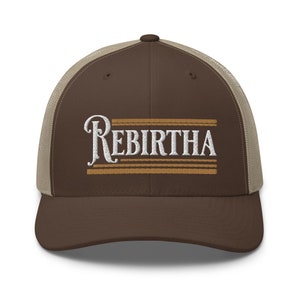 May include: A brown and beige trucker hat with the word "Rebirtha" embroidered in white on the front. The word is surrounded by four horizontal brown stripes.