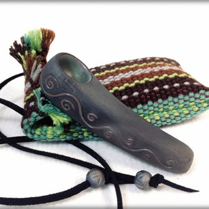 May include: A dark gray ceramic pipe with a swirling design, in a green and brown striped pouch with a black leather cord and beads.