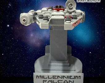 May include: A gray Millennium Falcon model on a pedestal stand. The stand has the words "MILLENNIUM FALCON" on the front. The image also includes the text "LEGO'S NOT INCLUDED" and "LEGO FLOATING WALL MOUNT W/PEDSTAL STAND".