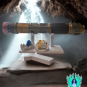 以下が含まれることがあります： 黒、金、銀のデザインが施された、詳細なライトセーバー。青いクリスタルと小さなプラークが付いた白いスタンドに展示されています。ライトセーバーはマルチカラーのエミッターを備え、洞窟の背景に設定されています。