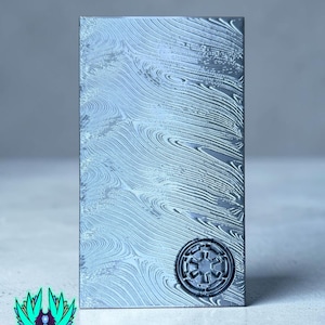 May include: A rectangular, silver metal bar with a swirling pattern and a raised Imperial symbol. The bar has a textured surface and is set against a light grey background. The logo "Jedi Forge" is in the lower left corner.