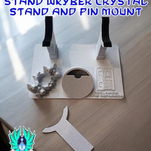 以下が含まれることがあります： 黒いアクセントが付いた白いライトセーバーのスタンド、クリスタルスタンド、ピンマウント。スタンドのテキストは「RECLAIMED AND REFORGED LIGHTSABER STAND WKYBER CRYSTAL STAND AND PIN MOUNT」と書かれています。画像にはロゴとハッシュタグ#GALACTICMERCANTILEGUILDも含まれています。