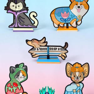 May include: A collection of six decorative acrylic character figures featuring a cat dressed as a villain, a corgi in a blue outfit, a dachshund inside a monorail, a cat in a green hood, a dog in a blue gown, and a logo reading JELZI FORGE.