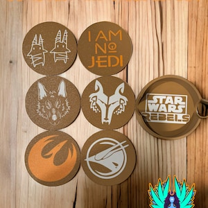 Könnte beinhalten: Satz mit sechs runden braunen Untersetzern mit verschiedenen Star Wars Rebels-Designs, darunter ein Rebellen-Symbol, ein Wolf und der Text "Ich bin kein Jedi". Ein brauner Halter mit dem Text "Star Wars Rebels" ist ebenfalls enthalten.