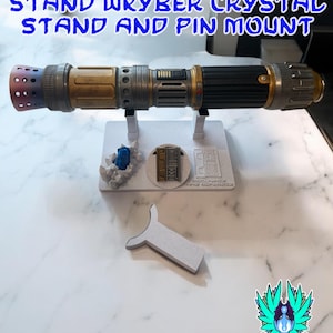 以下が含まれることがあります： 黒、金、銀色の柄のライトセーバーが、青いクリスタルとピンマウントが付いた白いスタンドに置かれています。「RECLAIMED AND REFORGED LIGHTSABER STAND WKYBER CRYSTAL STAND AND PIN MOUNT」というテキストが上部にあります。