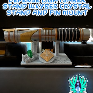 Puede incluir: Un soporte de sable de luz con un sable de luz dorado y plateado, un cristal kyber verde y un soporte gris con un montaje de pasador. El soporte tiene un diseño decorativo con un símbolo en el centro. El texto "#GALACTICMERCANTILEGUILD" está en la parte inferior de la imagen. La imagen también incluye un logotipo para "Jedi Forge Supply Co."