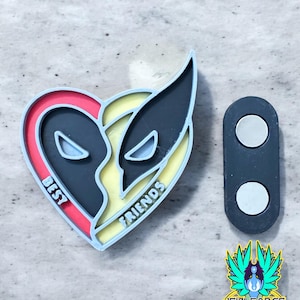 May include: A heart-shaped magnetic pin with a red and yellow design. The pin features the words "Best Friends" and the faces of Deadpool and Wolverine. The pin is attached to a black magnetic backing.
