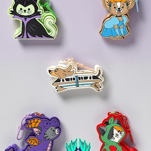May include: Five colorful character keychains featuring a cat dressed as a villain, a mouse in a blue dress, a dachshund inside a monorail, a cat in a purple dragon costume, and a cat in a red costume, plus a small logo reading JELZI FORGE.
