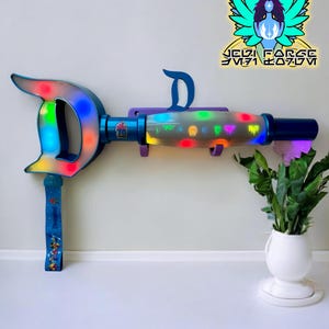 Könnte beinhalten: Ein blau-violetter Leuchtstab mit einem großen "D"-Design, das farbige Lichter aufweist. Der Stab hat einen Griff mit einem blauen Riemen und dem Text "Disneyland 70". Ein Logo mit der Aufschrift "Jedi Forge" befindet sich im Hintergrund.