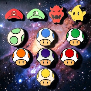 May include: A collection of colorful, cartoon-style character pins and mushroom-shaped pins. The pins feature various designs, including a red "M" hat, a green "L" hat, a Bowser character, a yellow star, and several mushroom designs with different colored spots.