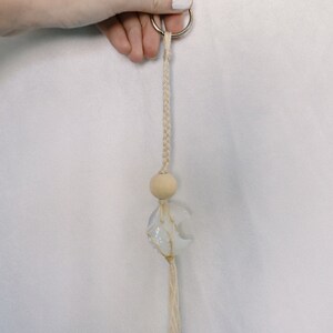 May include: A white and blue moon charm with a wooden bead and a white tassel hangs from a silver key ring.