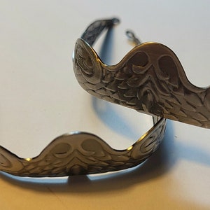 Pu&ograve; includere: Due decorazioni in metallo argentato a forma di corona con un design decorativo e ornato.