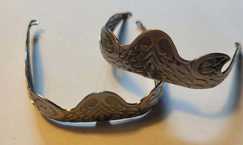 Pu&ograve; includere: Due decorazioni in metallo argentato a forma di corona con un design decorativo e ornato.