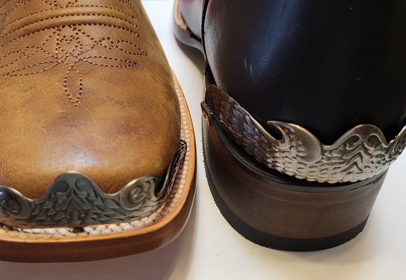 Pu&ograve; includere: Primo piano di due stivali da cowboy in pelle marrone con decorazioni in metallo argentato sulle dita. Gli stivali hanno una punta a punta e un design cucito sulla pelle.