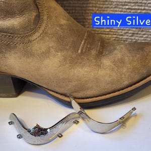 May include: A tan leather cowboy boot with a pointed toe and a metallic toe cap, positioned next to two separate shiny silver metal toe cap attachments. The text Shiny Silver is visible in a blue box near the top right of the image.