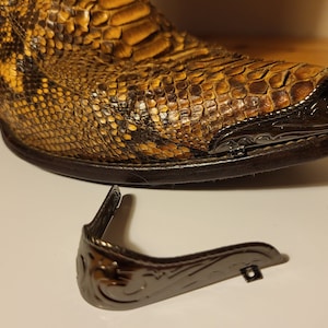 May include: A pair of brown snakeskin cowboy boots with a decorative metal toe cap and a separate metal spur strap.