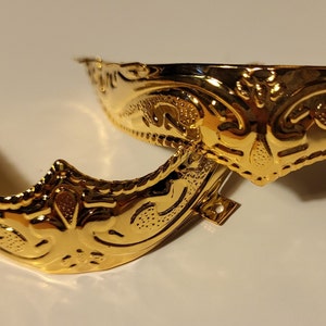 Op de afbeelding: Twee goudkleurige metalen schoensluitingen met sierlijke ontwerpen. De gespen zijn halfrond en hebben een decoratief patroon.
