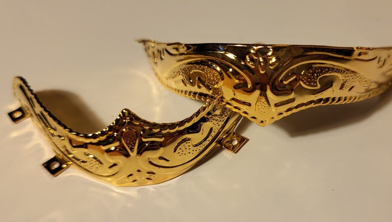 Op de afbeelding: Twee goudkleurige metalen schoensluitingen met sierlijke ontwerpen. De gespen zijn halfrond en hebben een decoratief patroon.