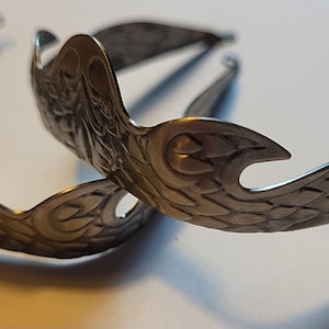Pu&ograve; includere: Due fermagli per capelli in metallo argentato con un design ornato con ali e motivi floreali.