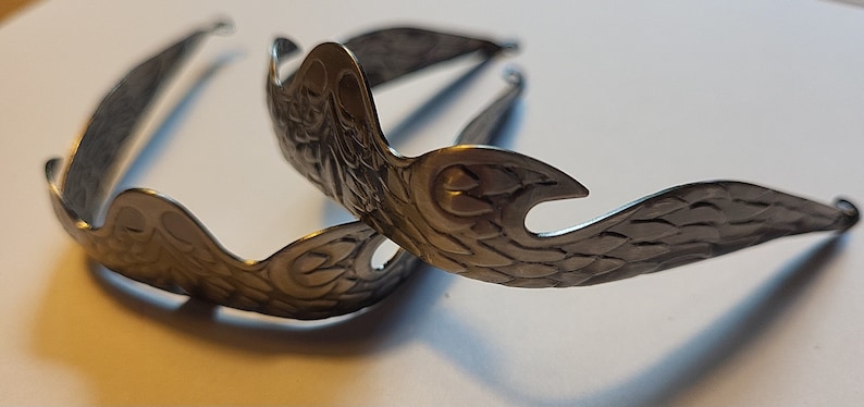 Pu&ograve; includere: Due fermagli per capelli in metallo argentato con un design ornato con ali e motivi floreali.