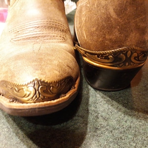 May include: A pair of brown leather cowboy boots with decorative metal accents. The boots have a pointed toe and a low heel.