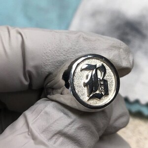 May include: A silver signet ring with a black letter 'B' engraved on the face.