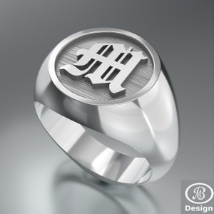 May include: A silver signet ring with a raised, circular design featuring the letter "M" in a bold, old English font.