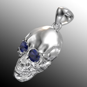 May include: Silver skull pendant with two blue gemstone eyes. The pendant has a loop at the top for attaching to a chain.