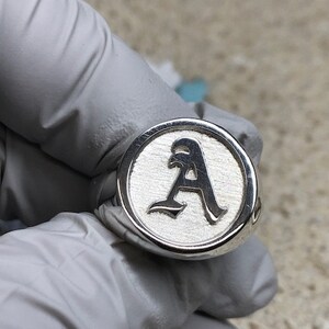 May include: A silver signet ring with a raised letter "A" in a gothic font.