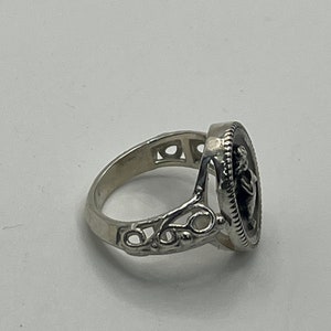 K&ouml;nnte beinhalten: Ein silberner Ring mit einem detaillierten Design, das einen runden Kamee mit dem Profil einer Frau zeigt. Der Ring hat ein zartes, filigranes Design.