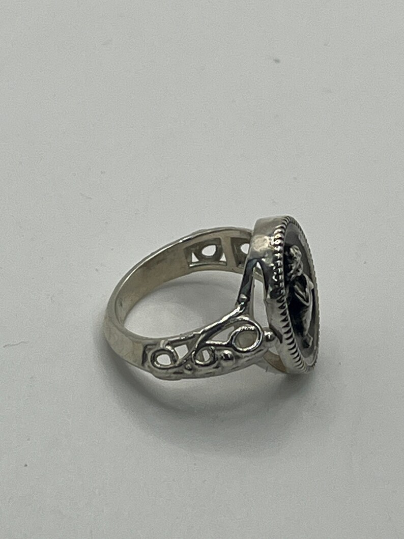K&ouml;nnte beinhalten: Ein silberner Ring mit einem detaillierten Design, das einen runden Kamee mit dem Profil einer Frau zeigt. Der Ring hat ein zartes, filigranes Design.