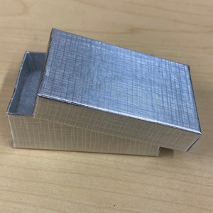 K&ouml;nnte beinhalten: Eine silberne Geschenkbox mit strukturierter Oberfl&auml;che. Die Box ist ge&ouml;ffnet und der Deckel ist abgewinkelt.