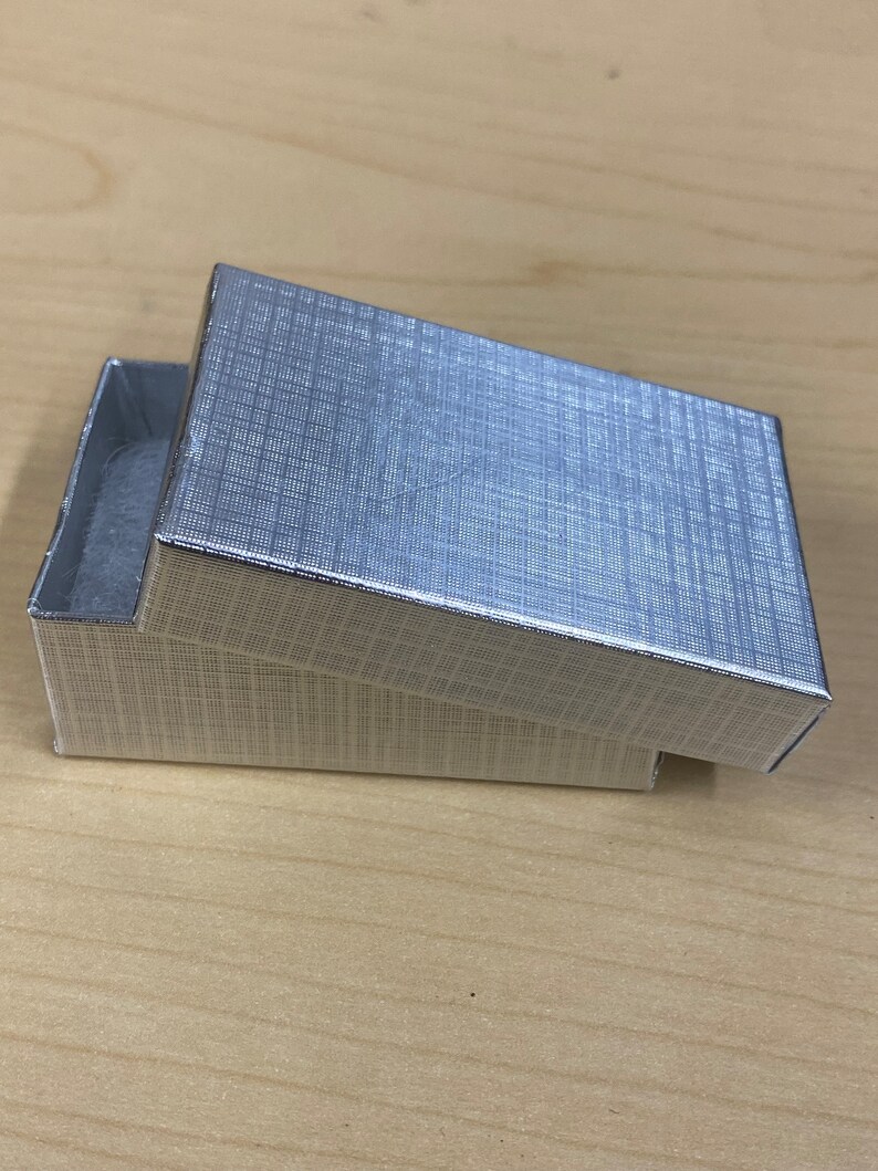 K&ouml;nnte beinhalten: Eine silberne Geschenkbox mit strukturierter Oberfl&auml;che. Die Box ist ge&ouml;ffnet und der Deckel ist abgewinkelt.