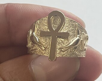 May include: A gold ring with an ankh symbol and two birds on either side. The ring is textured and has a polished finish.