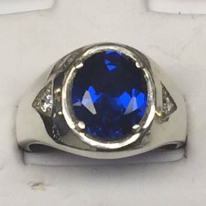 May include: A silver ring with a large oval blue gemstone and two smaller white gemstones on the sides.