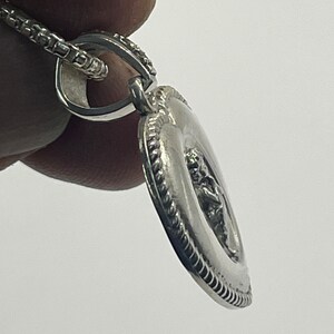 May include: Silver pendant necklace with a detailed design of a figure in a circle. The pendant is attached to a silver chain.