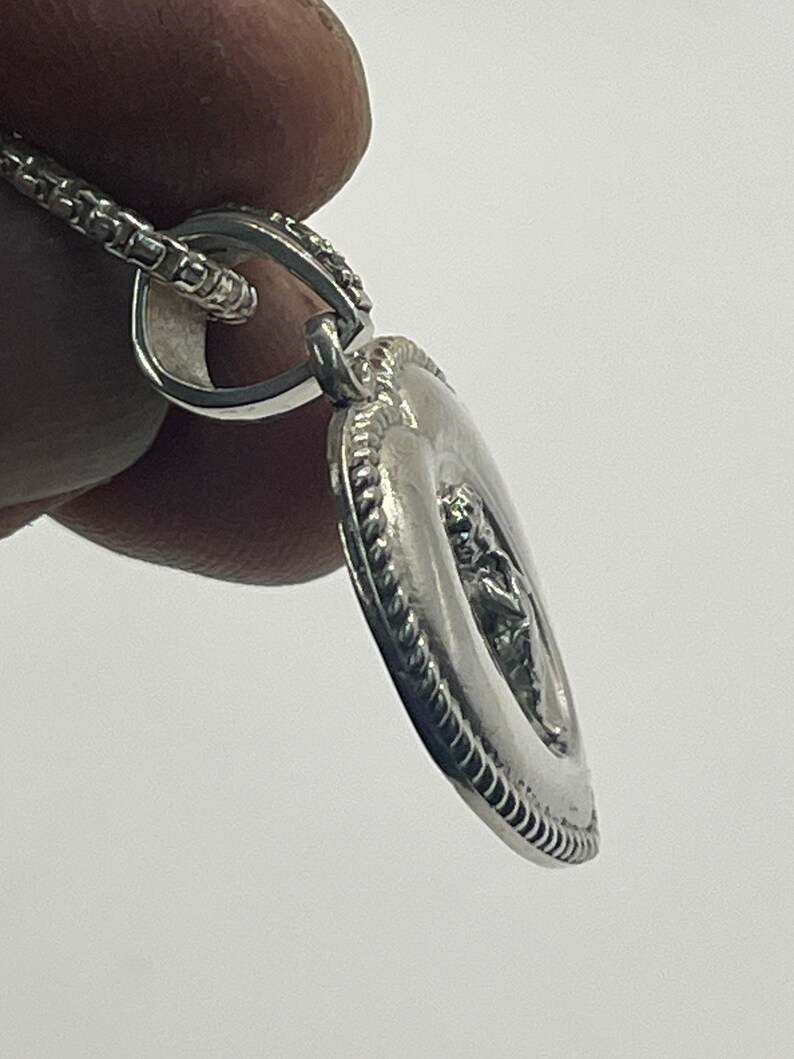 May include: Silver pendant necklace with a detailed design of a figure in a circle. The pendant is attached to a silver chain.