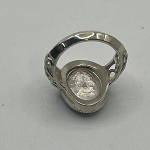 K&ouml;nnte beinhalten: Ein silberner Ring mit einem klaren ovalen Stein, der in einem filigranen Design gefasst ist.