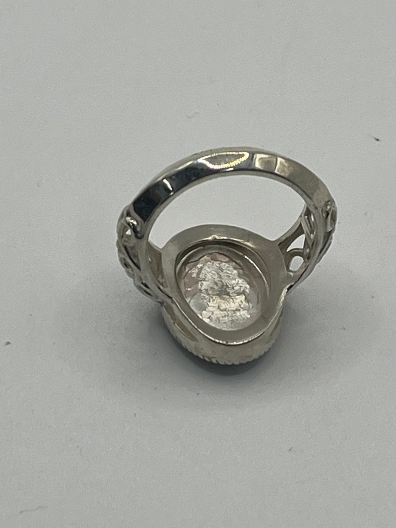 K&ouml;nnte beinhalten: Ein silberner Ring mit einem klaren ovalen Stein, der in einem filigranen Design gefasst ist.