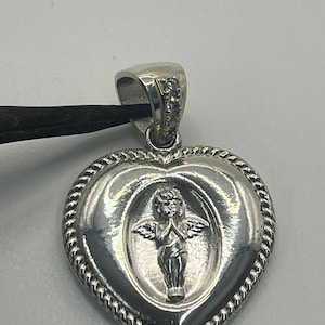 May include: Silver heart-shaped pendant with a detailed angel design and small clear stones on the bail.