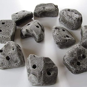 May include: A collection of gray climbing holds with various shapes and sizes. Each hold has multiple pre-drilled holes for mounting. The holds are made of a textured material, resembling natural rock formations, and are designed for indoor or outdoor climbing.