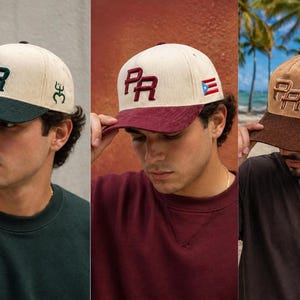 May include: Baseball caps in three color combinations. The caps have a corduroy texture with a contrasting bill. Each cap features the letters "PR" embroidered on the front, with a small flag on the side. The caps are worn by a person.