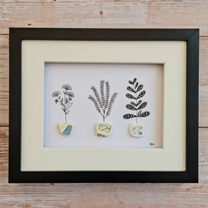 Puede incluir: Una obra de arte enmarcada con tres dibujos en blanco y negro de plantas en macetas de cerámica. Las macetas están decoradas con patrones azules y blancos.