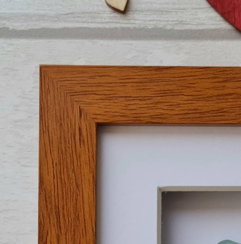 May include: A close-up of the top corner of a wood picture frame. The frame is a light brown color with a wood grain texture. The frame is empty and ready for a picture.