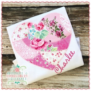 May include: A white t-shirt with a pink patchwork heart applique and the name "Charlie" embroidered on the front. The heart is made of various pink floral fabrics.