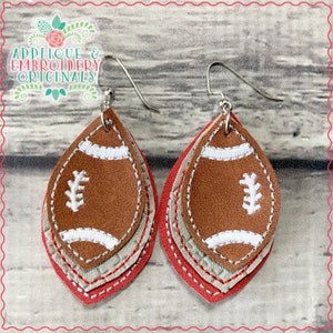 May include: A pair of layered leather earrings featuring a brown football design with white stitching. The earrings are layered with red, gray, and brown leather.
