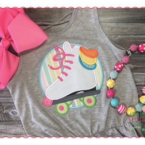 Könnte beinhalten: Ein graues Tanktop mit einem aufgestickten weißen Rollschuh. Der Rollschuh ist von einem Kreis mit einem Regenbogenstreifenmuster umgeben. Das Tanktop wird mit einer bunten Perlenkette kombiniert.