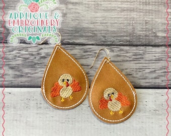 May include: A pair of brown leather teardrop-shaped earrings with gold hooks. Each earring features an embroidered image of a small, orange and white turkey.
