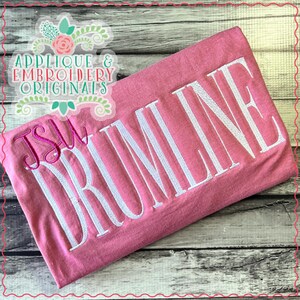 May include: Pink t-shirt with white embroidery that reads "Drumline" and "JSW".