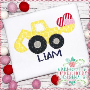 May include: A yellow toy construction vehicle with a red and white heart in the bucket. The vehicle has black wheels and a name, "LIAM", embroidered below it.
